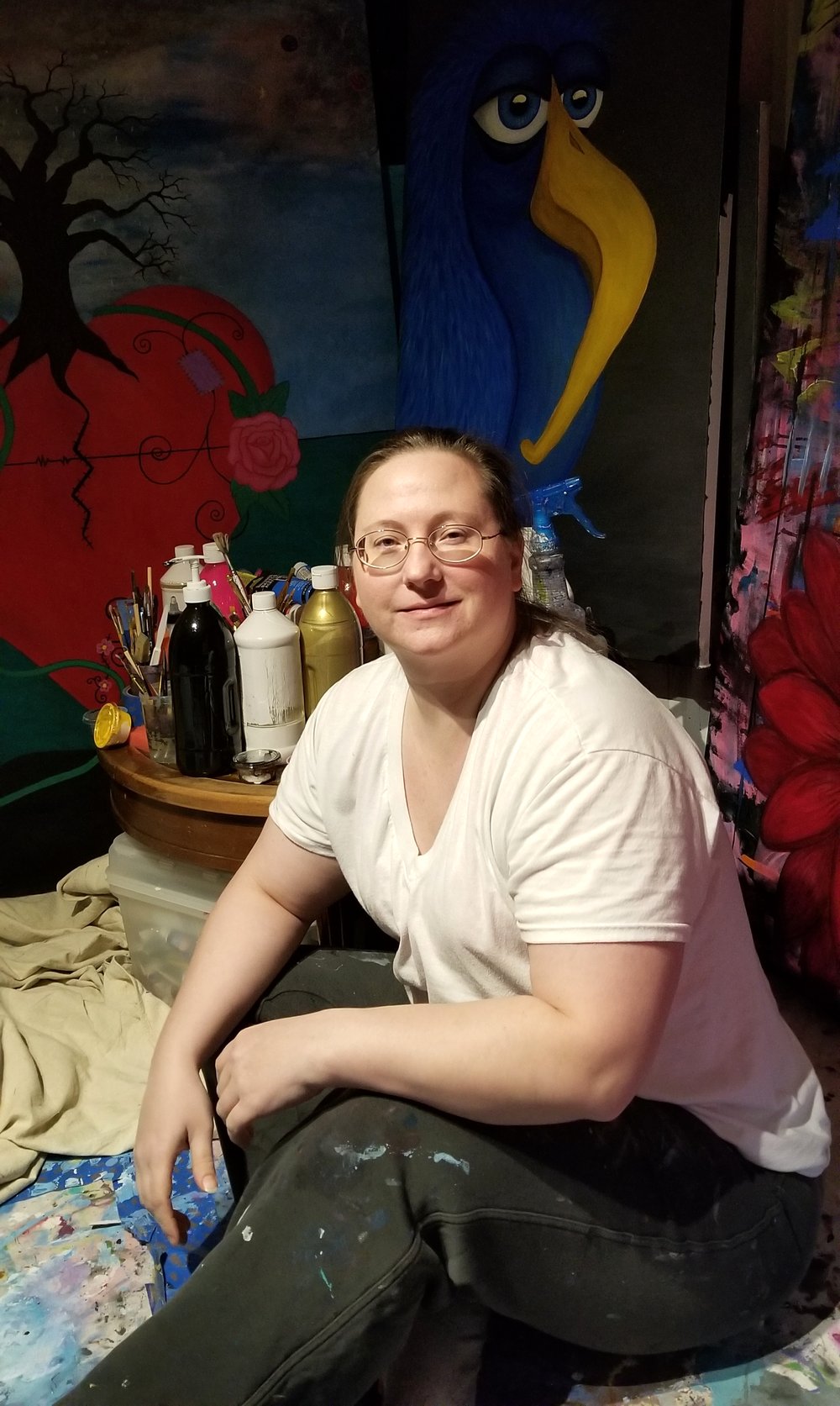 Kristy Lewellen seated in her art studio surrounded by paintings and paint supplies